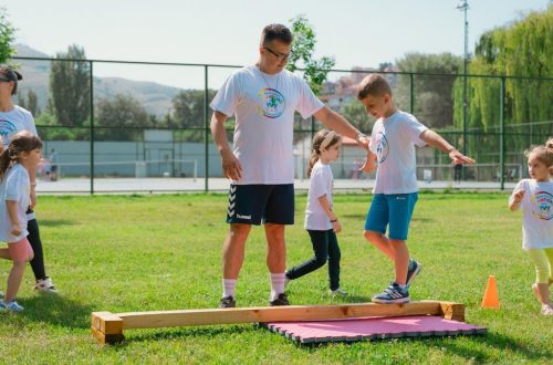Kids guided by instructors at a park balance on a beam for fun and exercise.